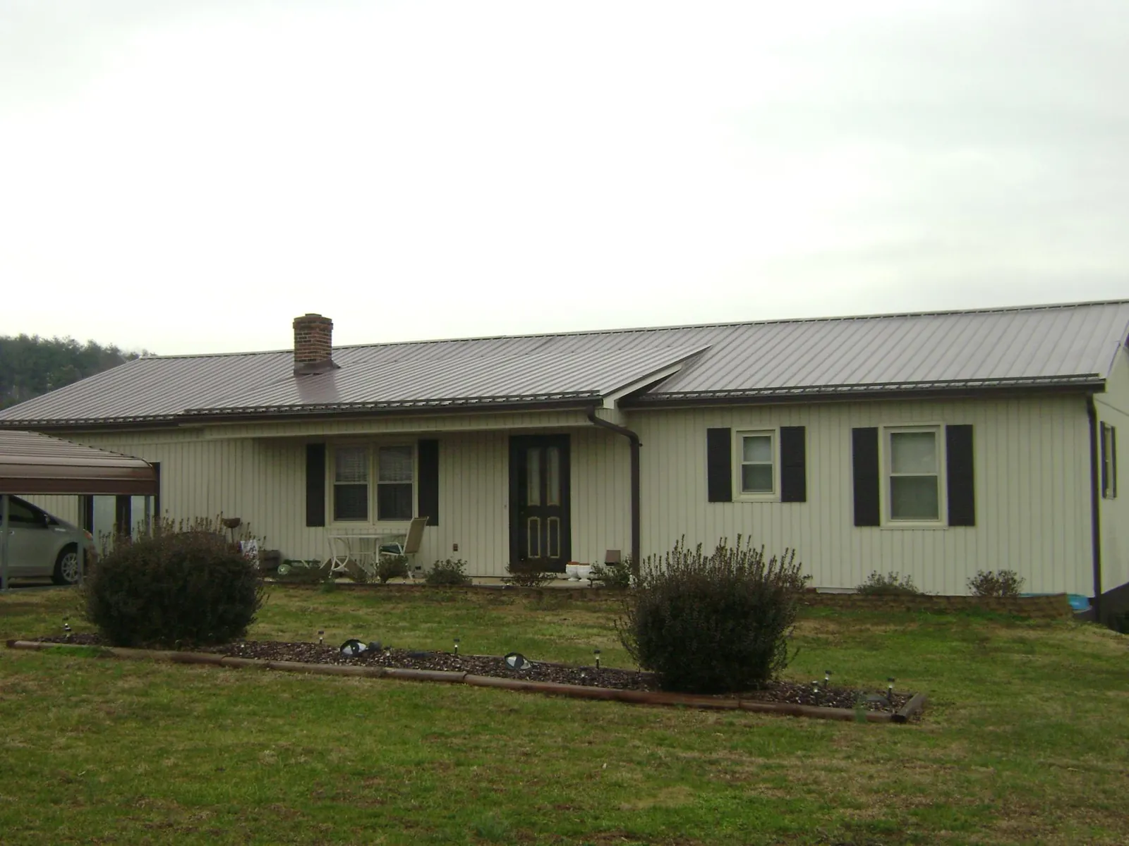 Brown metal roof on a cream sided ranch home with a brick chimney in Rockville