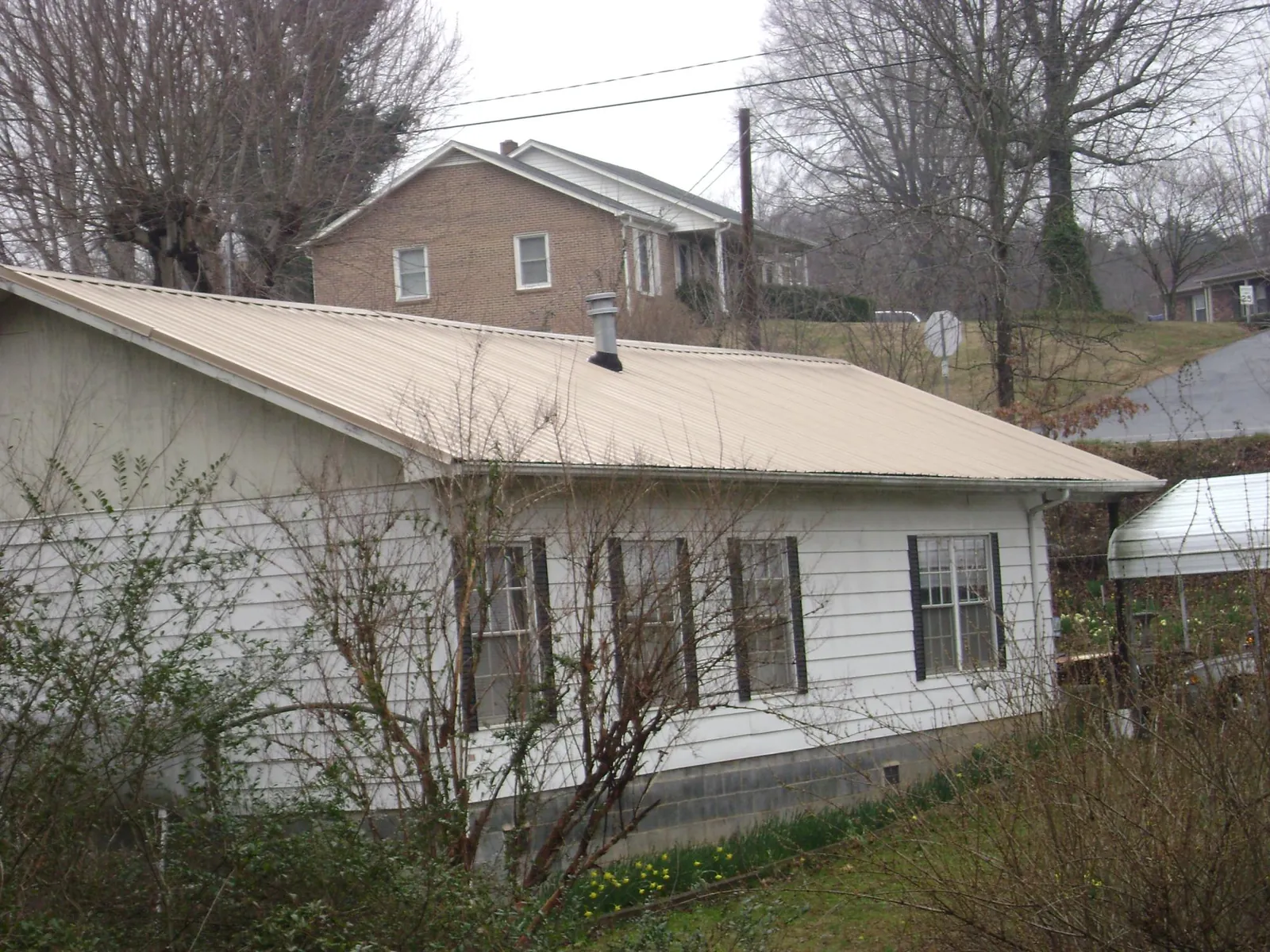 Tan metal roof on a white sided house set into a hillside — Commercial Roofing by Roofing Brothers in Rockville